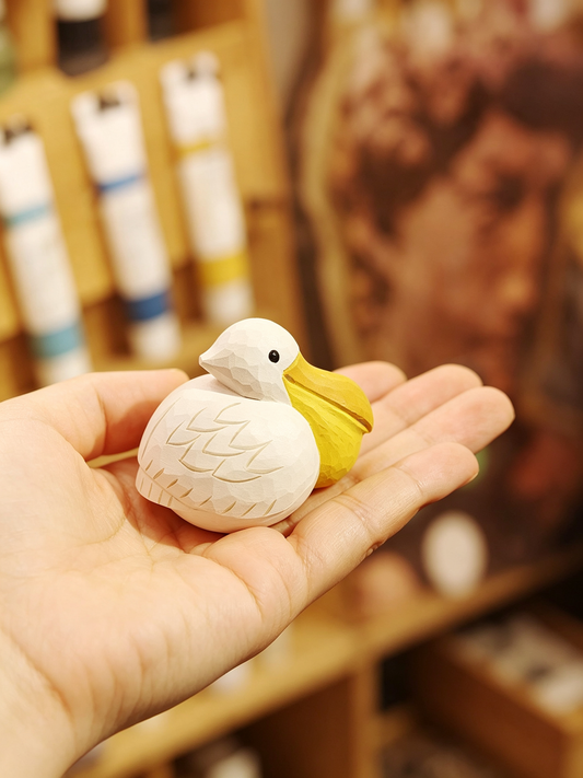 Mini hand-carved linden wood Pelican figurine resting on an open palm, showing the consistent pale warm wood tone of the natural oil finish.