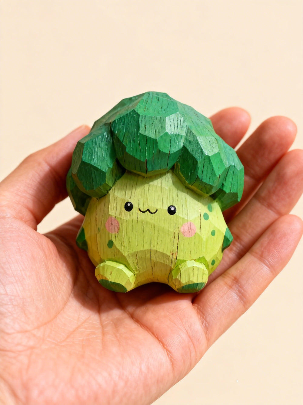 Hand-carved wooden broccoli figurine with a cute face held in an open hand against a cream background, showing its palm-sized scale by PINEAURA